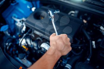 Worker in uniform disassembles vehicle engine, car service station. Automobile checking and inspection, professional diagnostics and repair