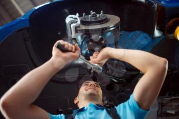 Worker in uniform repairing vehicle on lift, car service station. Automobile checking and inspection, professional diagnostics and repair