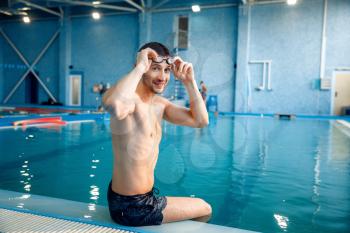 Male swimmer in swimming glasses poses in pool. The man at the poolside, aqua aerobics instructor poses in the water