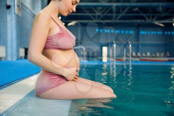 Pregnant woman with big belly swimming in the pool indoors. Pregnancy being, relaxation in the water, recreational exercise for health care