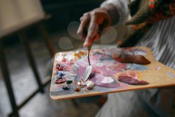 Male painter holds brush and colorful paints on palette, art studio. Artist draws at his workplace
