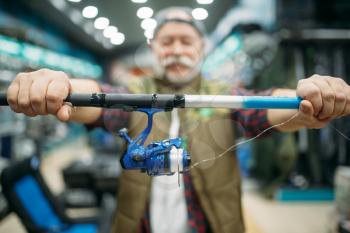 Male angler shows rod with reel in fishing shop. Equipment and tools for fish catching and hunting, accessory choice on showcase in store, spinnings and telescopes assortment
