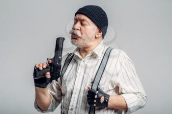 Elderly man with gun isolated on grey background, gangster. Mature senior in hat holds weapon, robber in old age