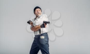 Elderly man poses with gun on grey background, gangster. Mature senior in hat holds weapon, robber in old age