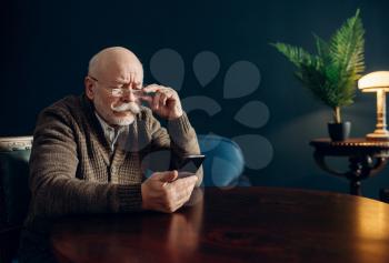 Elderly man using mobile phone in home office. Bearded mature senior with smartphone in living room, old age businessman