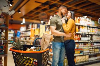 Love family couple hugs in grocery store. Man and woman with cart buying beverages and products in market, customers shopping food and drinks