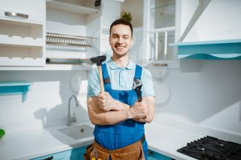Cheerful male plumber in uniform holds wrench and plunger in the kitchen. Handyman with toolbag repair sink, sanitary equipment service at home