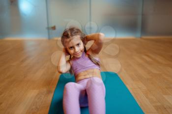 Little girl doing press exercise on mat in gym, fitness workout. Female kid in sportswear, child on training in sport club