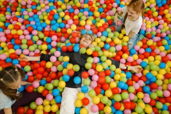 Children with mother lying among colorful balls in the entertainment center. Mom and her daughter leisures on holidays, childhood happiness, happy kids on playground