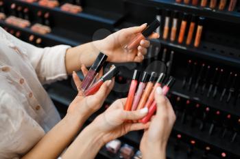 Cosmetician and woman holds nail varnish at the showcase in cosmetics store. Luxury beauty shop salon, female customer and beautician in fashion market