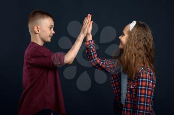 Little boy and girl beats the palms in studio. Happy childhood, children having fun, funny kids isolated on dark background, child emotion