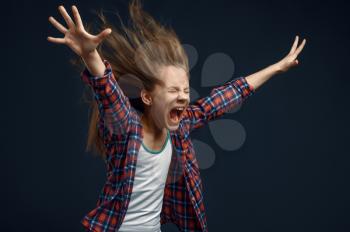 Little girl screams in studio, developing hairstyle effect. Children and wind, kid isolated on dark background, child emotion