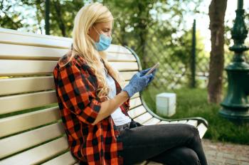 Young woman in mask sitting on bench in park, quarantine. Female person walking during the epidemic, health care and protection, pandemic lifestyle