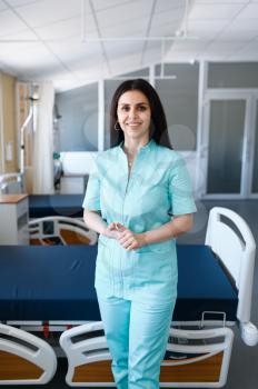 Smiling female surgeon poses at the bed in clinic, surgery. Doctor in uniform, medical worker, medicine and health, professional healthcare in hospital