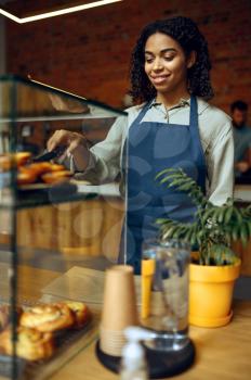 Female barista in apron holds plate with croissant in cafe. Woman choosing sweets in cafeteria, waiter at the counter in bar