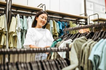 Woman choosing clothes in clothing store. Female person shopping in fashion boutique, shopper looking on garment