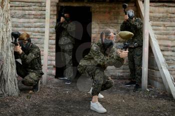 Paintball team in camouflages and masks fights on playground in the forest. Extreme sport with pneumatic weapon and paint bullets or markers, military game outdoors, combat tactics