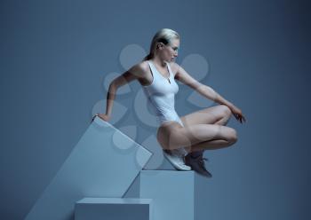 Model in white clothes and futuristic glasses lying on cubes, light grey background. Female person in virtual reality style, future technology