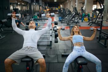 Fit couple doing exercise with dumbbells, fitness training in gym. Athletic man and woman on workout in sport club, active healthy lifestyle, physical wellness