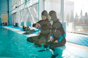 Woman and male divemaster in scuba gear preparing for the dive, diving school. Teaching people to swim underwater, indoor swimming pool interior on background