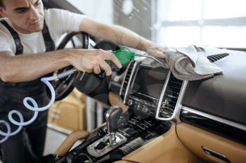 Worker with air gun cleans car air duct grating, dry cleaning and detailing. Vehicle washing in garage, thoroughly care of automobile