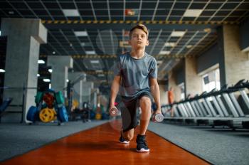 Boy doing exercise with dumbbells in gym. Youngster on training in sport club, health care and healthy lifestyle, schoolboy on workout