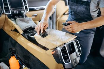 Worker with brush wipes car armrest, dry cleaning and detailing. Vehicle washing in garage, thoroughly care of automobile, chemical and vacuum clean service