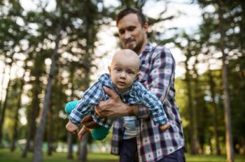 Father play with his little baby in summer park. Dad with male kid on lawn, picnic with child on plaid in the forest, family happiness