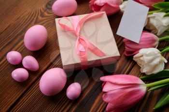 Pink tulips, easter eggs and gift box on wooden background. Spring flowers blooming and paschal food, fresh floral decoration, holiday celebration symbol