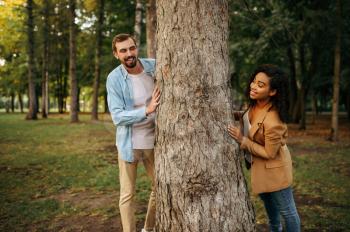 Love couple poses at the big tree, romantic walking in the park. Man and woman relax outdoors, green lawn on background. Family relax on the meadow in summertime, weekend in nature