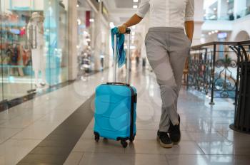 Woman with suitcase poses at the showcase in mall. Female traveler with luggage in shopping center, passenger with bag in tax free market. Girl with baggage