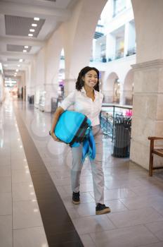 Happy woman carries suitcase in tax free market. Female traveler with luggage in shopping center, passenger with bag in mall. Girl with baggage