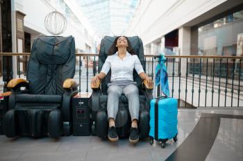 Woman with suitcase relax in massage chair, airport waiting hall. Female person with luggage, international air gate, passenger with bag. Girl with baggage in departure terminal