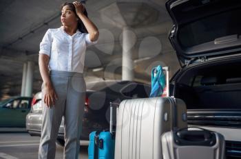 Young woman with suitcases in a panic, car parking. Female traveler with luggage in vehicle park lot, passenger with many bags. Girl with baggage near automobile
