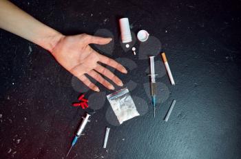 Drug addict woman hand, syringe, pills and powder in zip package, black table on background. Narcotic addiction problem, eternal depression of junky people, junkie concept