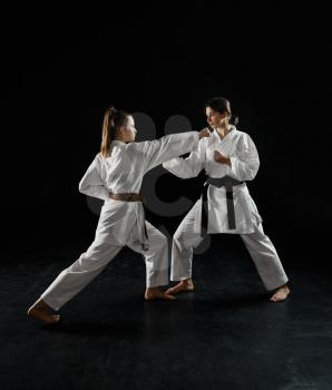 Two female karatekas in white kimono, strike in action, dark background. Karate fighters on workout, martial arts, women fighting competition