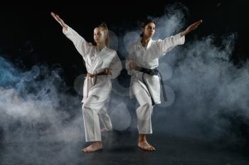 Female karatekas in white kimono, combat stance in action, dark background. Karate fighters on workout, martial arts, women fighting