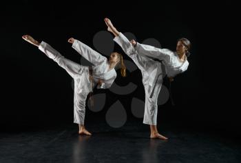 Female karatekas in white kimono, combat stance in action, dark background. Karate fighters on workout, martial arts, women fighting competition