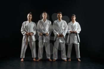 Four karatekas in white kimono, group training, dark background. Karate fighters on workout, martial arts, fighting competition