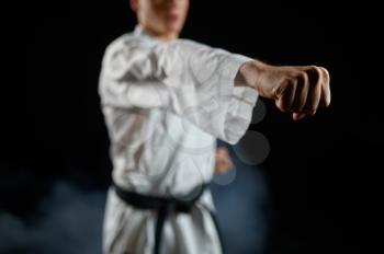 Male karateka, fighter practice in white kimono, combat stance, dark background. Man on karate workout, martial arts, training before fighting competition
