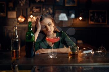 Depressed woman drinks different alcohol at the counter in bar. One female person in pub, human emotions, leisure activities, nightlife