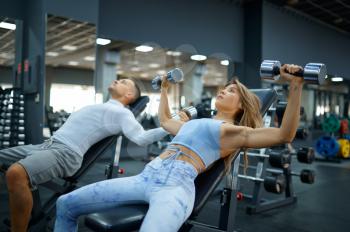 Fit couple doing exercise with dumbbells, fitness training in gym. Athletic man and woman on workout in sport club, active healthy lifestyle, physical wellness