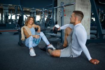 Couple relax on the floor after fitness training in gym. Athletic man and woman on workout in sport club, active healthy lifestyle, physical wellness