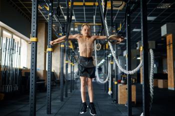 Athletic boy doing exercise on rings in gym. Youngster on training in sport club, healthcare and healthy lifestyle, schoolboy on aerobics workout, sportive youth