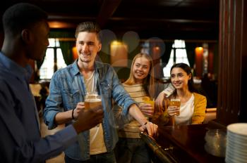 Friends with beer make a toast at the counter in bar. Group of people relax in pub, night lifestyle, friendship, event celebration