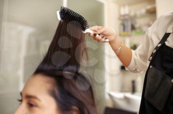 Hairdresser works with comb, female customer at the mirror in hairdressing salon. Stylist and client in hairsalon. Beauty business, professional service