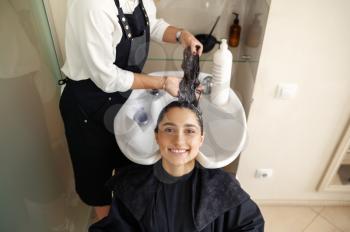 Hairdresser washes woman's hair, side view, hairdressing salon. Stylist and client in hairsalon. Beauty business, professional service