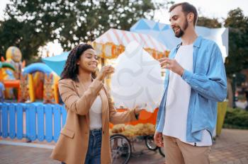 Love couple eating cotton candy in city amusement park. Man and woman relax outdoors. Family leisures in summertime, entertainment theme