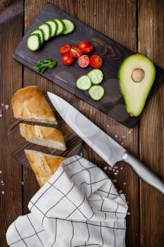 Fresh cutted vegetables and avocado on board on wooden background. Organic vegetarian food, grocery assortment, natural products, healthy lifestyle concept