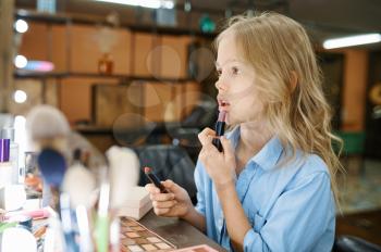 Little girl applies pomade at the mirror in makeup salon. Mom and daughter play stylists together, happy childhood, glamour family, young make-up artist or hairdresser